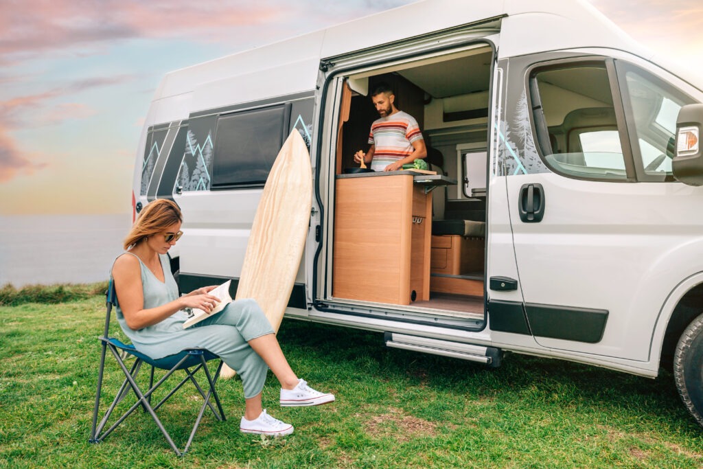 man-cooking-vegetables-camper-van-while-woman-reads-outdoors (2)